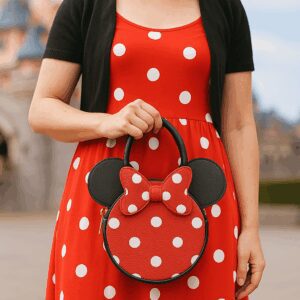 Person Disneybounding as Minnie Mouse with a red polka-dot dress and Minnie handbag in front of Sleeping Beauty Castle at Disneyland Paris