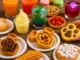 A vibrant table filled with colourful snacks and drinks, including waffles, churros, cookies, pastries, fruit, ice cream, and assorted juices—perfect for a family-friendly snack guide in 2025.