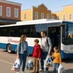 A real family with children carrying Disney shopping bags, boarding a Disneyland Paris free shuttle bus outside a Western-themed Disney hotel inspired by Hotel Cheyenne, with the hotel in the background on a sunny day.