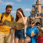 A real family of four at Disneyland Paris in summer, looking confused with a park map, a child in a rain poncho and sunglasses, and spilled popcorn near Sleeping Beauty Castle, showing classic theme park mistakes.